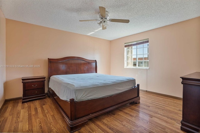 bedroom with a ceiling fan, wood finished floors, baseboards, and a textured ceiling