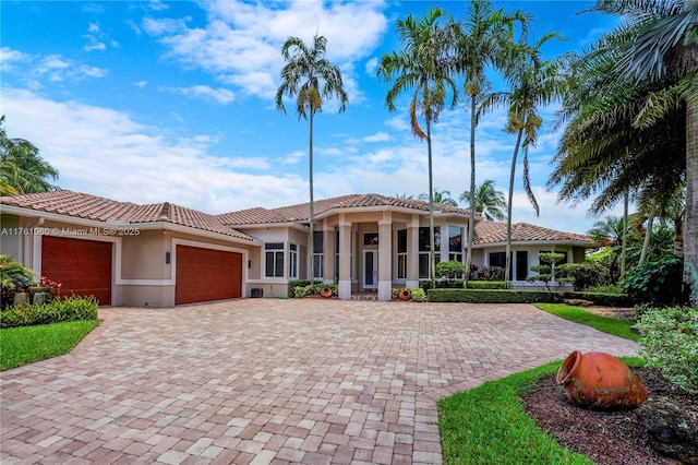 mediterranean / spanish home featuring decorative driveway, stucco siding, an attached garage, and a tiled roof