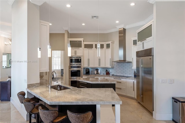 kitchen with visible vents, a sink, built in appliances, wall chimney exhaust hood, and tasteful backsplash