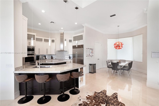 kitchen with wall chimney range hood, built in appliances, ornamental molding, decorative backsplash, and a peninsula