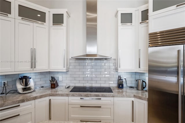 kitchen with black electric stovetop, high end fridge, wall chimney exhaust hood, and white cabinets