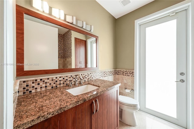 bathroom featuring vanity, a wainscoted wall, visible vents, tile walls, and toilet