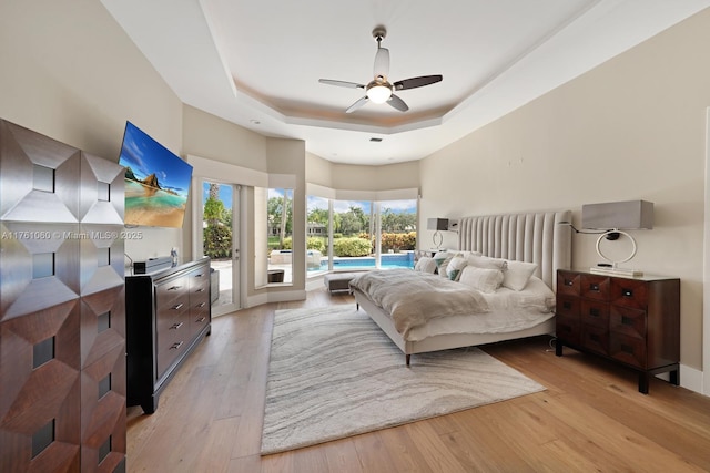 bedroom with a tray ceiling, access to outside, light wood-style floors, and ceiling fan