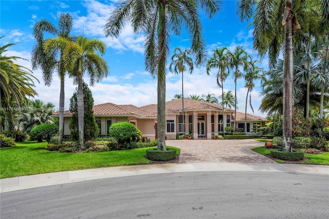 mediterranean / spanish-style home with decorative driveway, a tile roof, a front yard, and stucco siding