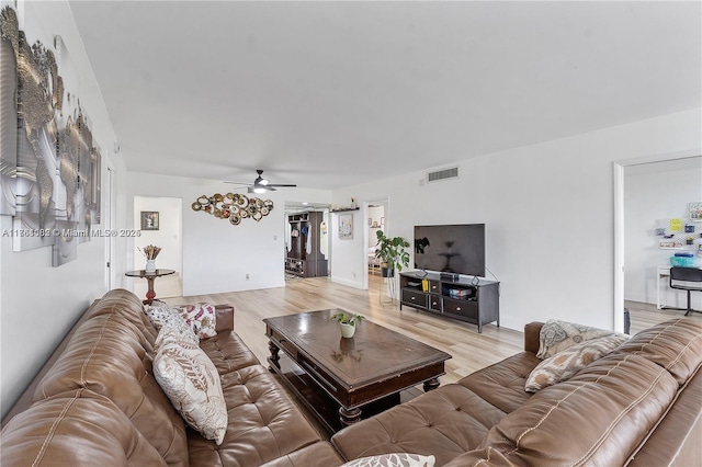 living room featuring light wood-type flooring, visible vents, and a ceiling fan