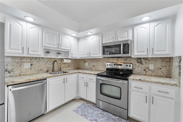 kitchen with a sink, light stone counters, appliances with stainless steel finishes, and light tile patterned floors