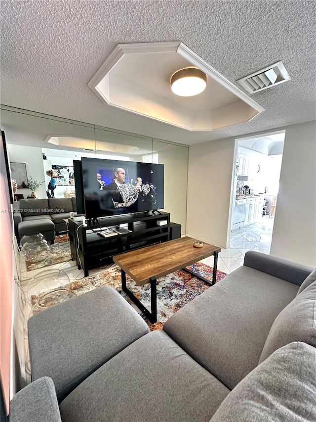 living area featuring tile patterned floors, visible vents, a textured ceiling, and a tray ceiling