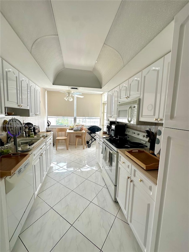 kitchen featuring white appliances, lofted ceiling, ceiling fan, a sink, and white cabinets