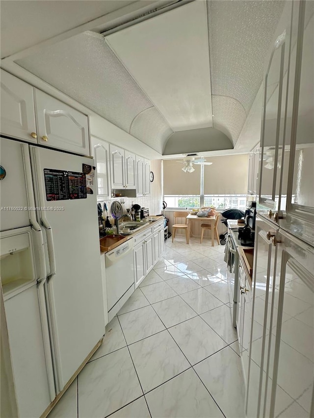 kitchen with white appliances, a ceiling fan, vaulted ceiling, white cabinetry, and dark countertops