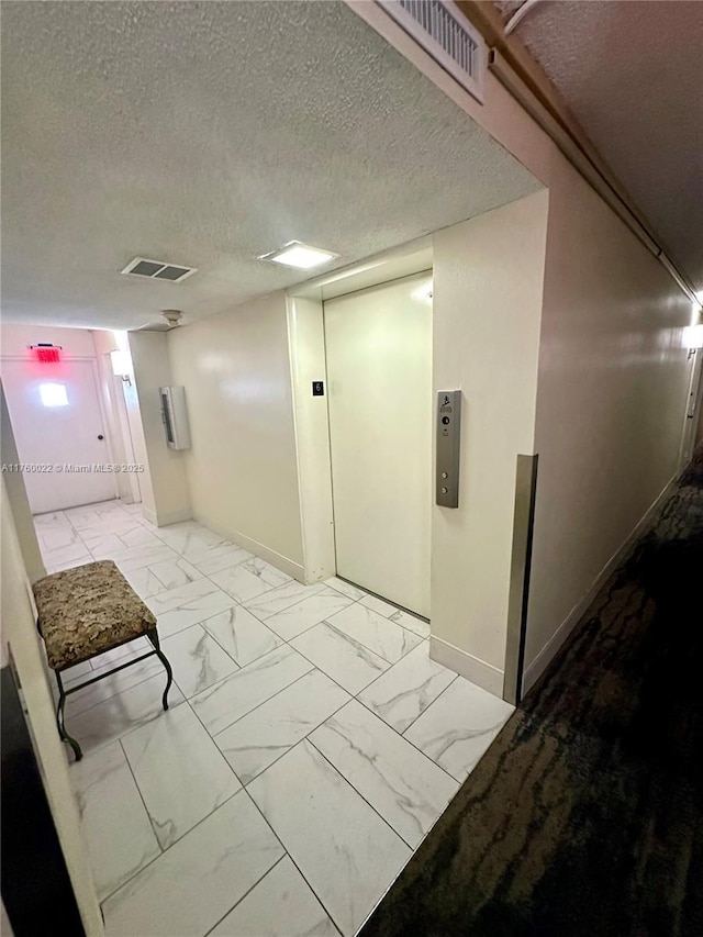 hallway with visible vents, marble finish floor, a textured ceiling, and baseboards