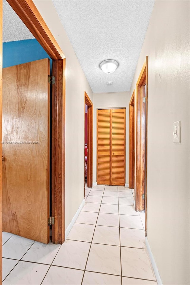 hall with light tile patterned floors, baseboards, and a textured ceiling