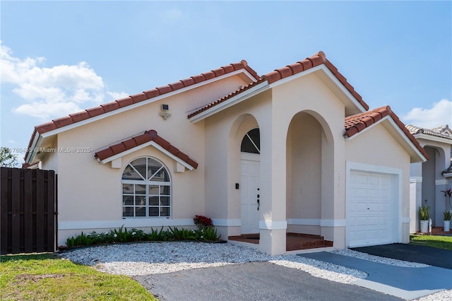 mediterranean / spanish-style house with stucco siding, driveway, an attached garage, and fence