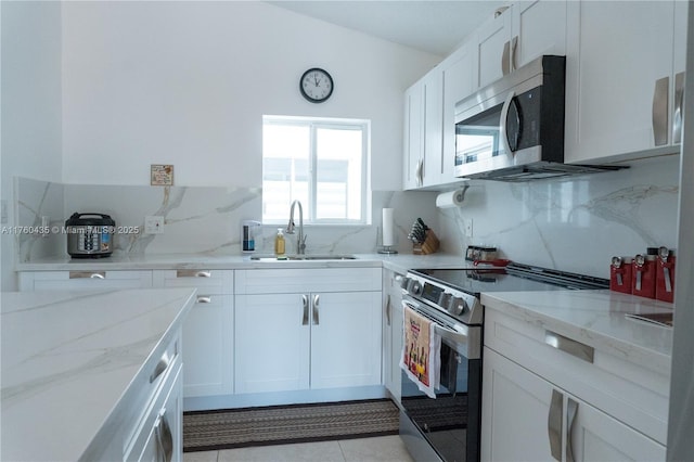 kitchen featuring light stone countertops, a sink, decorative backsplash, appliances with stainless steel finishes, and white cabinetry