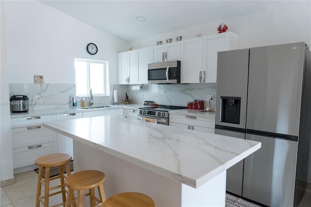 kitchen with backsplash, a kitchen bar, stainless steel appliances, white cabinetry, and a sink