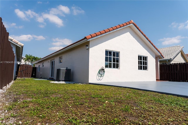 view of side of home with a patio, cooling unit, fence, a yard, and stucco siding