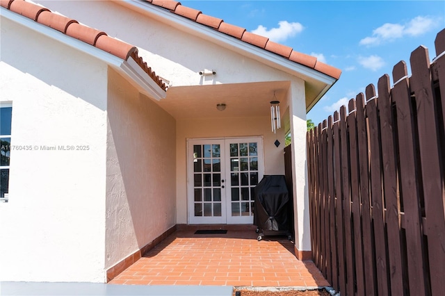 entrance to property featuring a tile roof, french doors, fence, and stucco siding