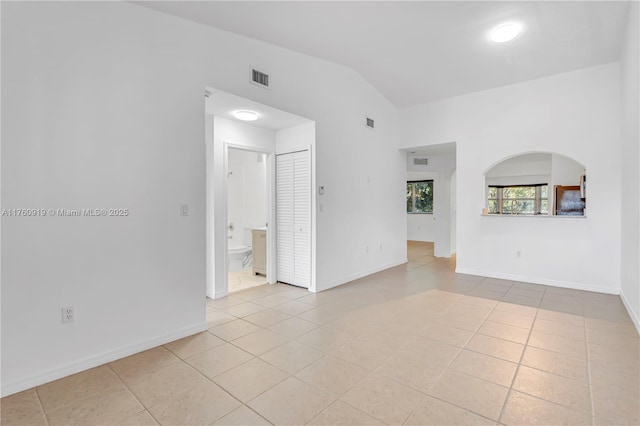 empty room featuring light tile patterned floors, baseboards, lofted ceiling, and visible vents