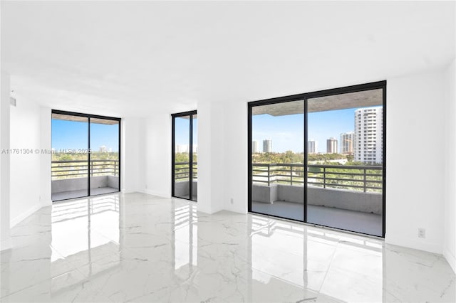 unfurnished room featuring a wall of windows, a city view, baseboards, and marble finish floor