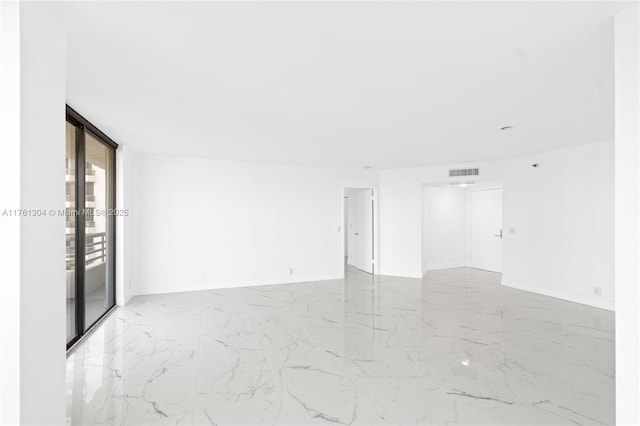 empty room featuring a wall of windows, baseboards, visible vents, and marble finish floor