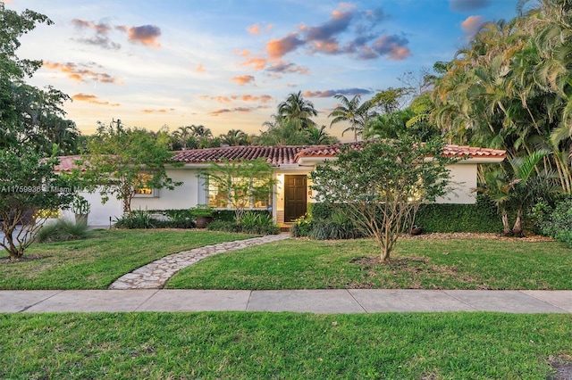 mediterranean / spanish home featuring stucco siding, a tiled roof, and a front lawn