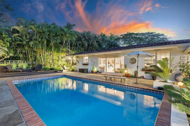 back of house at dusk with an outdoor pool, stucco siding, and a patio area