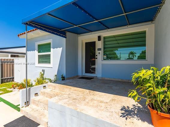 doorway to property featuring stucco siding and fence