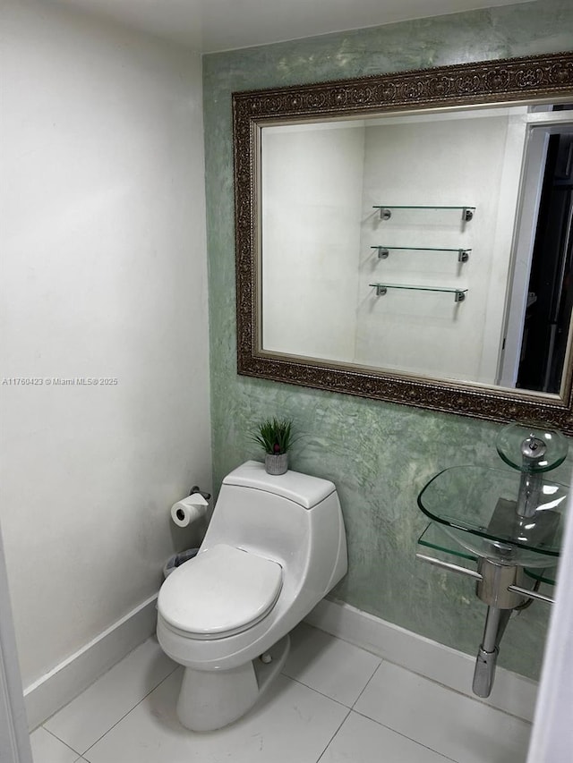 half bath featuring tile patterned floors, toilet, and baseboards