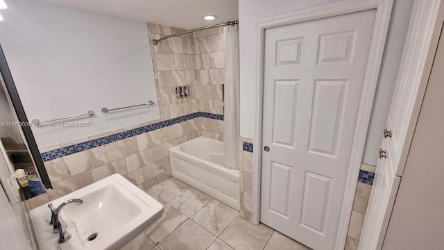 bathroom featuring tile walls, shower / bath combination with curtain, marble finish floor, and a sink