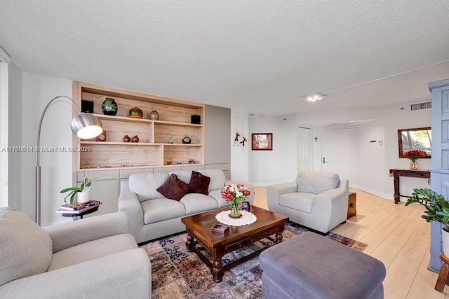 living area featuring baseboards, light wood-style floors, visible vents, and a textured ceiling