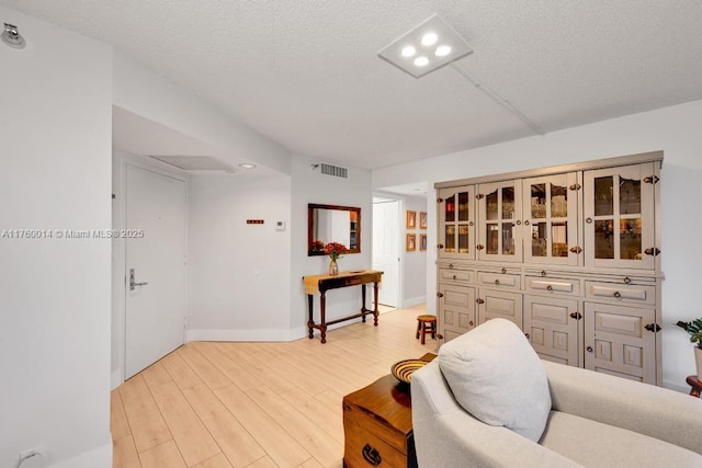 sitting room with light wood finished floors, visible vents, a textured ceiling, and baseboards