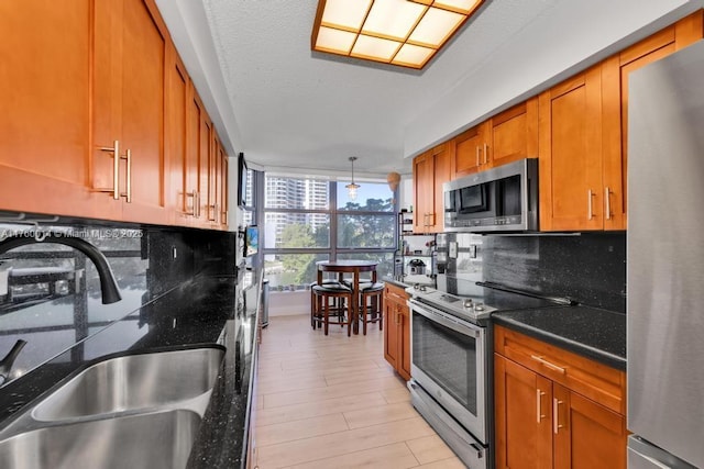 kitchen with brown cabinets, a sink, dark stone countertops, tasteful backsplash, and appliances with stainless steel finishes