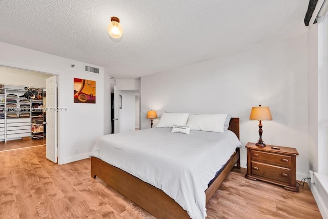 bedroom with visible vents, a textured ceiling, a walk in closet, and light wood-style floors