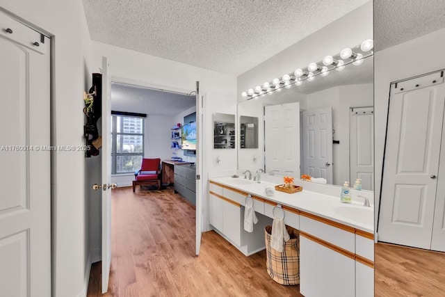 ensuite bathroom with wood finished floors, double vanity, a sink, ensuite bathroom, and a textured ceiling