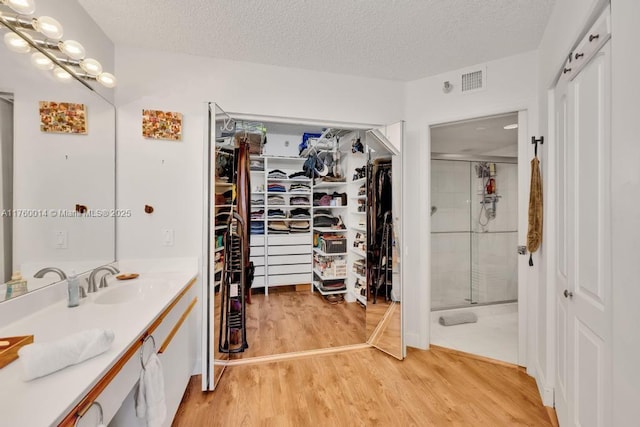 full bath featuring a walk in closet, a textured ceiling, wood finished floors, a shower stall, and vanity