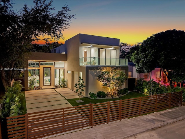 modern home featuring a balcony, a fenced front yard, and stucco siding