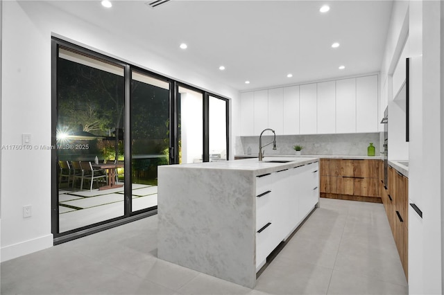 kitchen with a wall of windows, a sink, white cabinets, modern cabinets, and tasteful backsplash