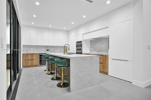kitchen with wine cooler, modern cabinets, light countertops, and a sink