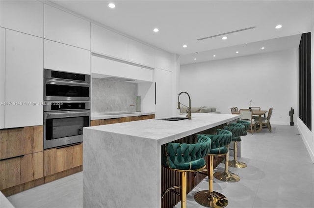 kitchen featuring modern cabinets, a sink, a kitchen breakfast bar, stainless steel double oven, and cooktop