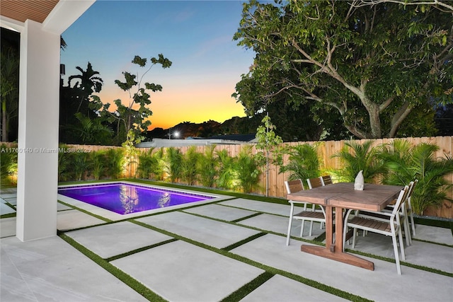 pool at dusk featuring outdoor dining space, a patio area, a fenced in pool, and a fenced backyard