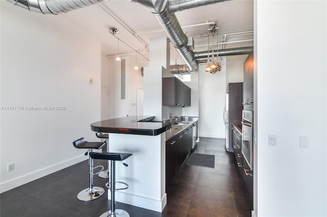 kitchen featuring baseboards, appliances with stainless steel finishes, dark countertops, a kitchen breakfast bar, and modern cabinets