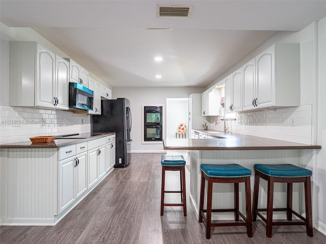 kitchen with visible vents, black appliances, a breakfast bar, a sink, and dark wood-style flooring