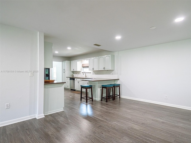 kitchen with dark wood-type flooring, baseboards, a breakfast bar, white cabinets, and stainless steel dishwasher