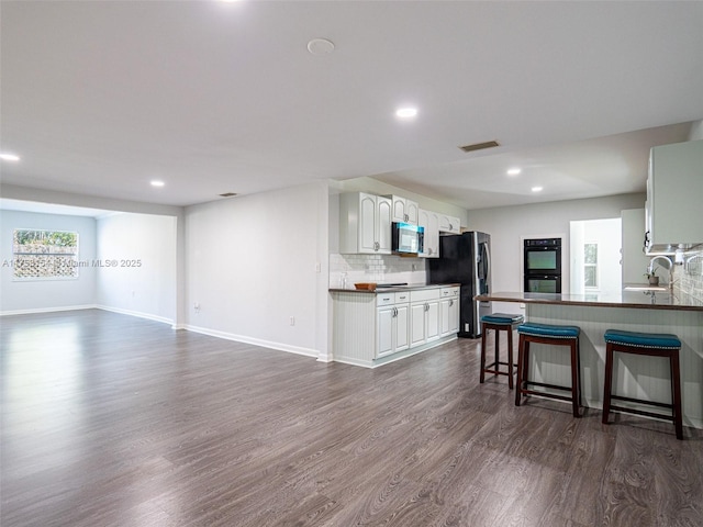 kitchen featuring dark countertops, backsplash, a breakfast bar area, appliances with stainless steel finishes, and dark wood-style flooring