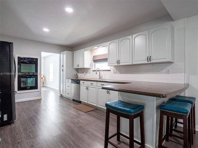 kitchen with a breakfast bar, freestanding refrigerator, a sink, dobule oven black, and stainless steel dishwasher