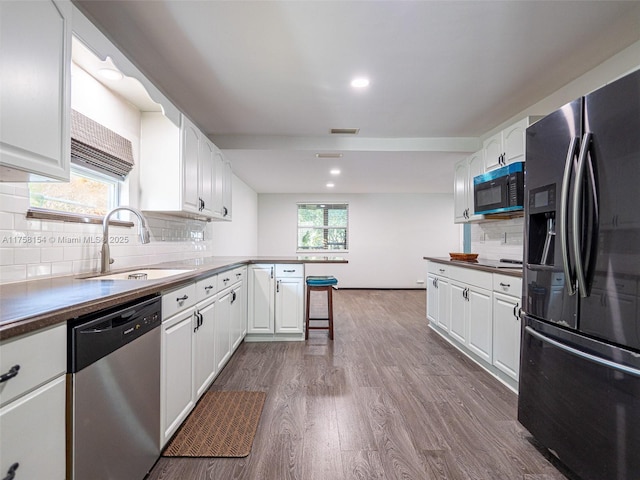 kitchen featuring visible vents, a peninsula, dark wood-style flooring, a sink, and appliances with stainless steel finishes