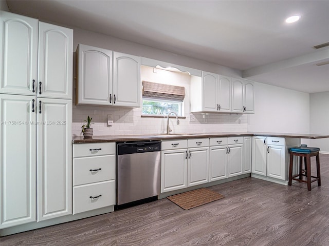 kitchen with tasteful backsplash, a peninsula, stainless steel dishwasher, dark wood-style floors, and a sink