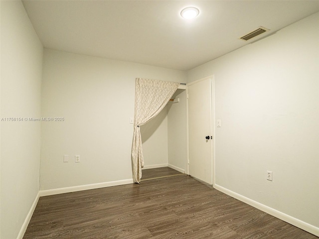 spare room with dark wood-style floors, visible vents, and baseboards