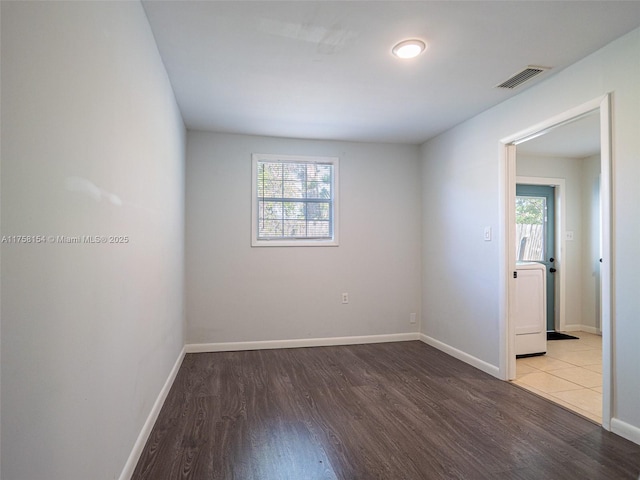 unfurnished room featuring washer / clothes dryer, wood finished floors, visible vents, and baseboards