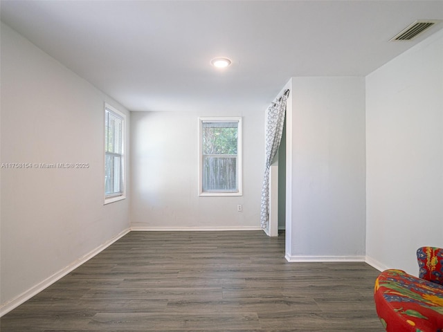 unfurnished room featuring a wealth of natural light, visible vents, and dark wood-style flooring