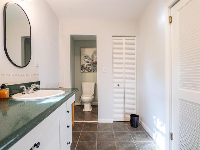 bathroom featuring vanity, toilet, baseboards, and a closet